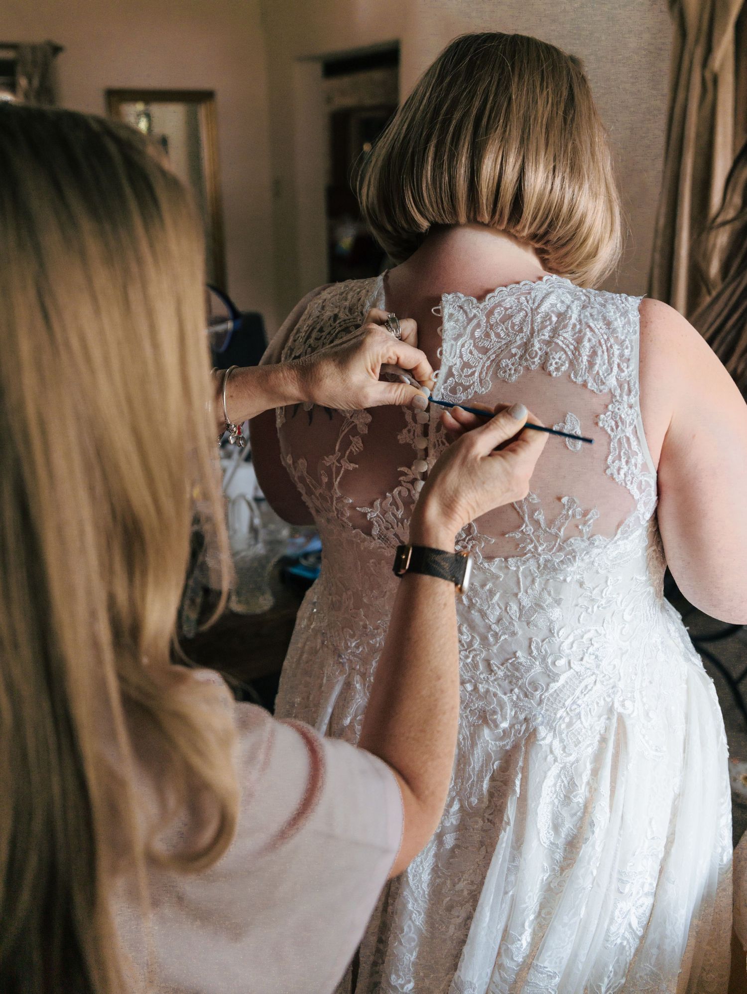 Someone helping to button up the back of an elegant white lace wedding dress in a getting ready sequence.