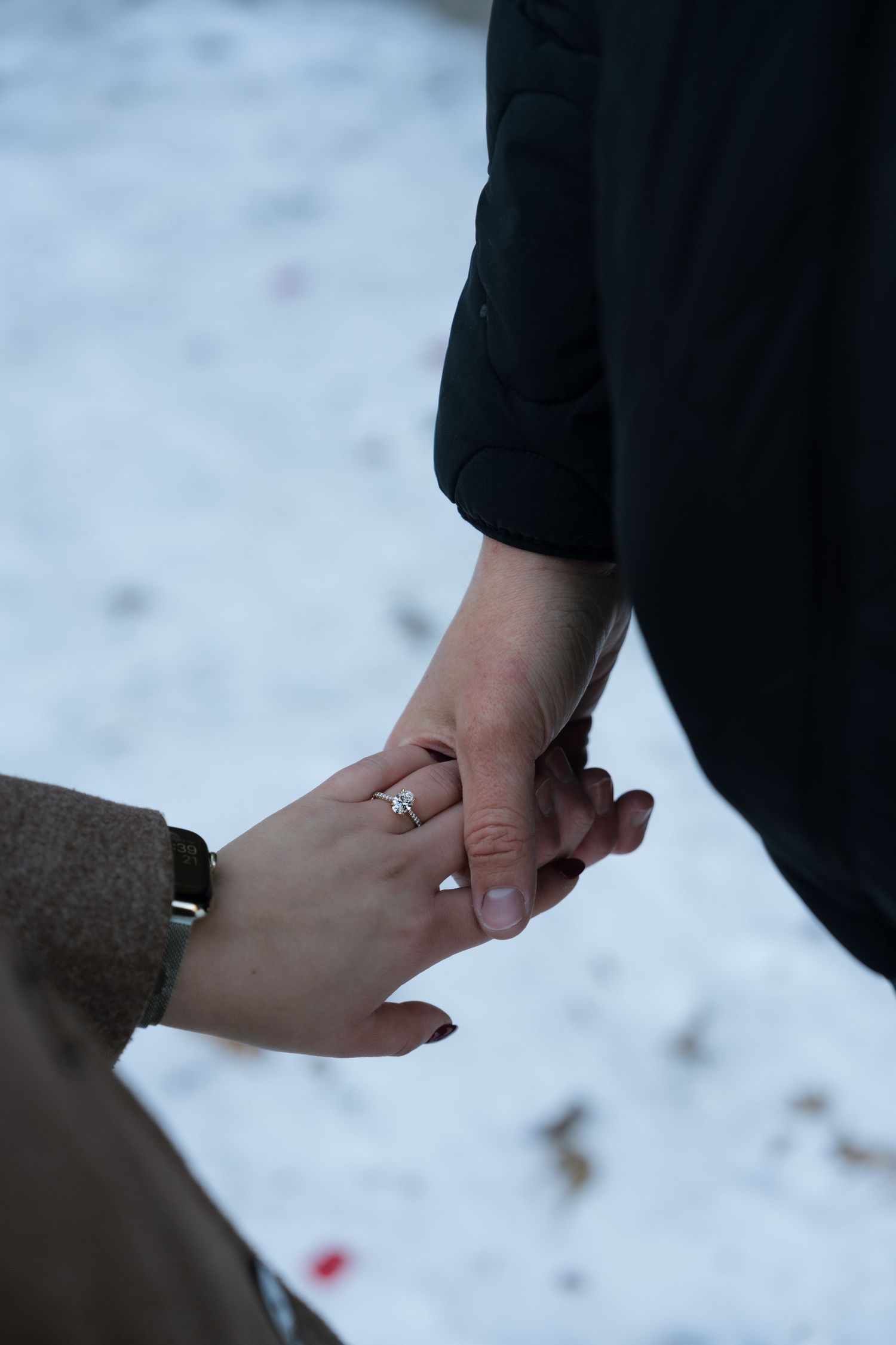 Close-up of hands holding each other with an engagement ring visible in a romantic moment.