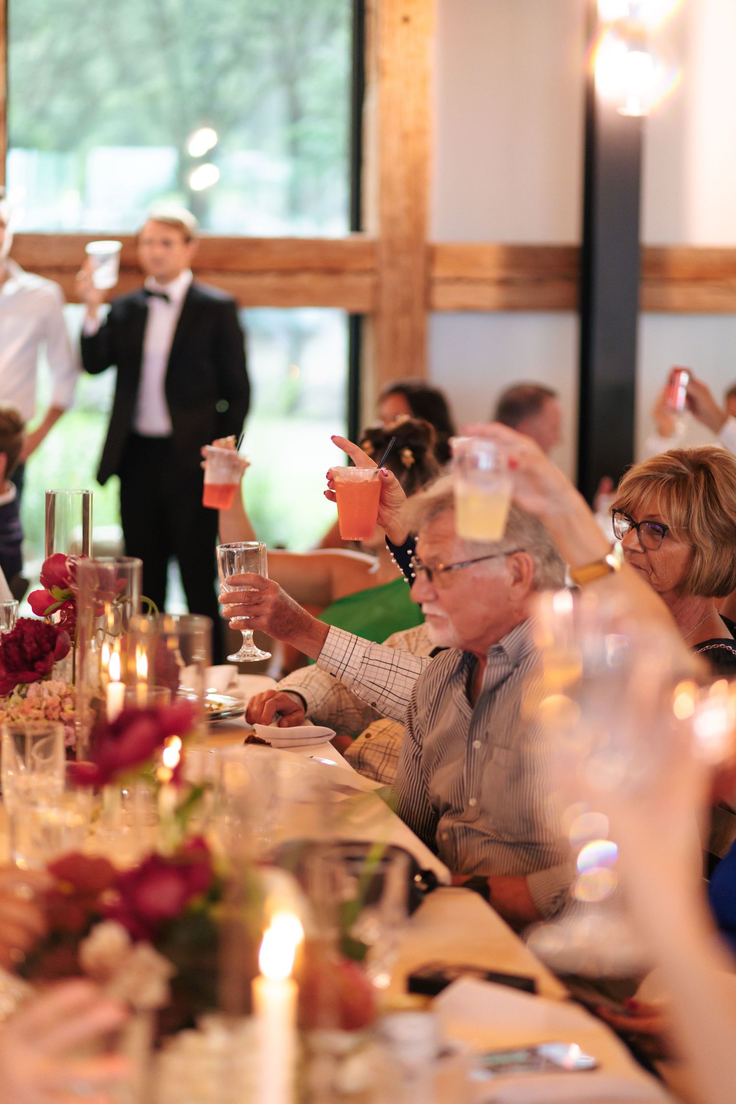 Wedding reception dinner table decorated with red flowers and candlelight in rustic venue.