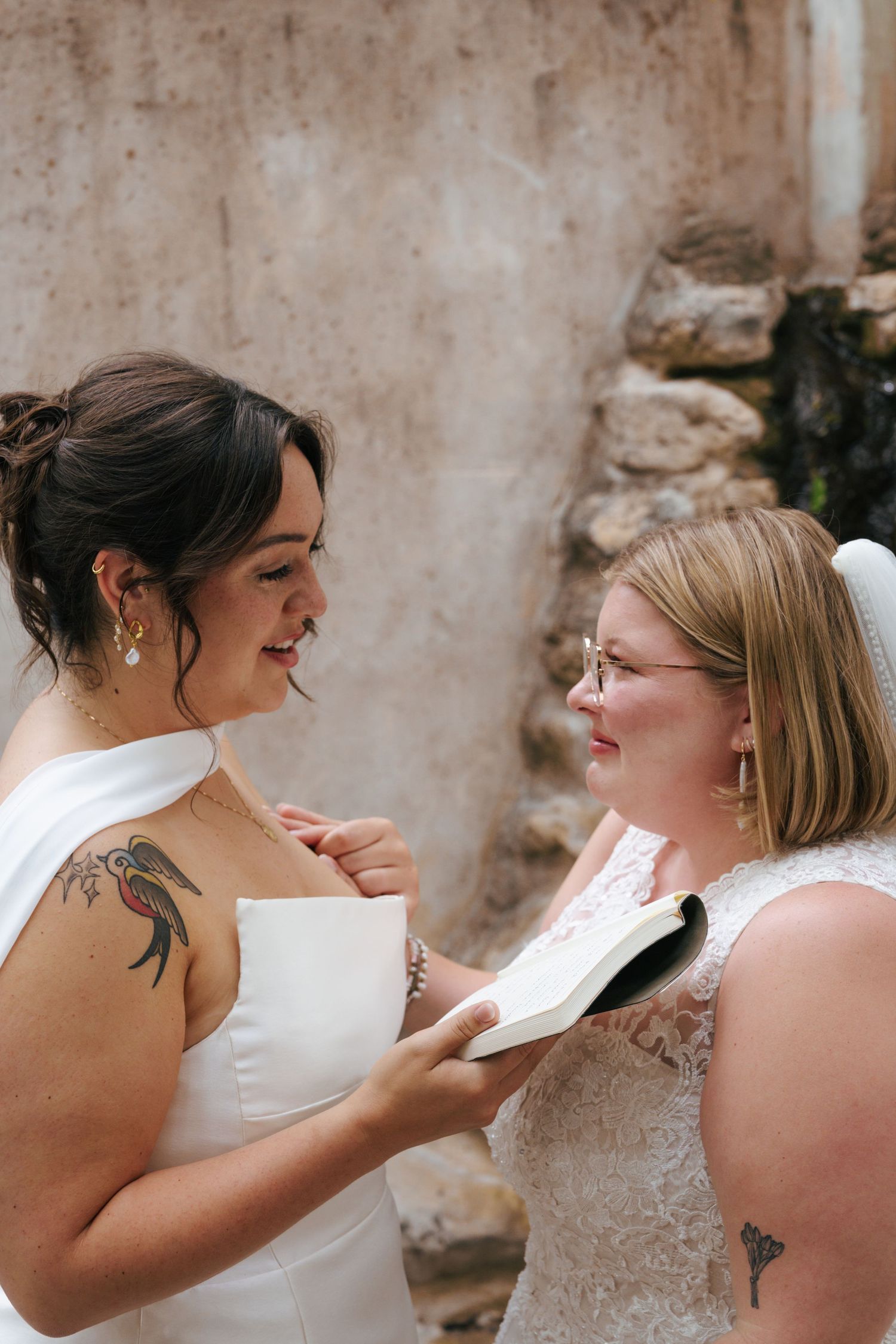 Two brides share intimate moments in a series of candid wedding photos against a rustic stone wall.