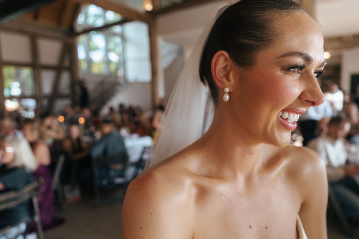 Candid wedding reception moment captured in a rustic venue with exposed wooden beams.