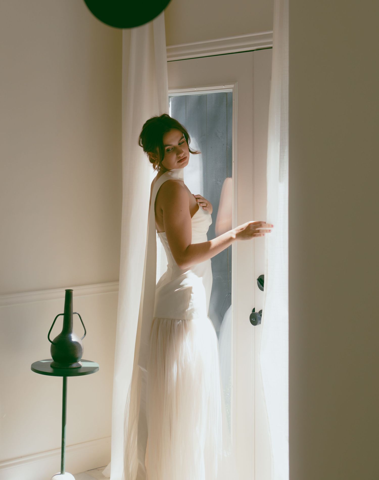 Soft, dreamy window light illuminates a white dress against interior walls.
