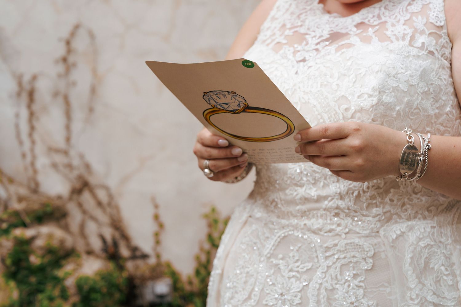 Close-up of hands in white lace wedding dress holding a handwritten note with a heart illustration.