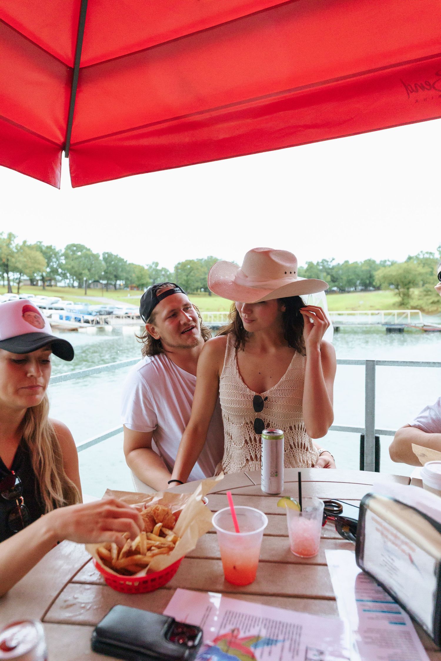 Group enjoying casual outdoor dining with french fries and drinks under a red awning by the waterfront.