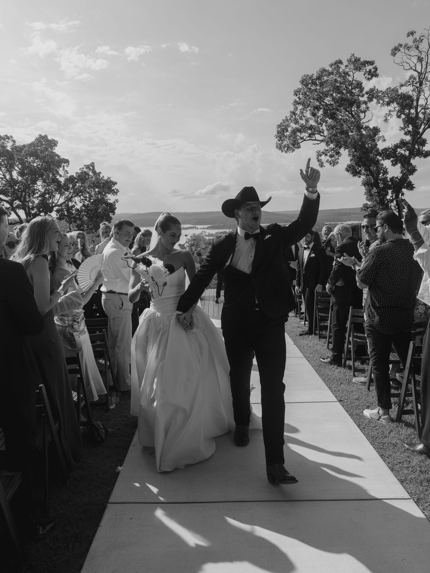 Wedding party members raise their arms in celebration on an outdoor walkway.