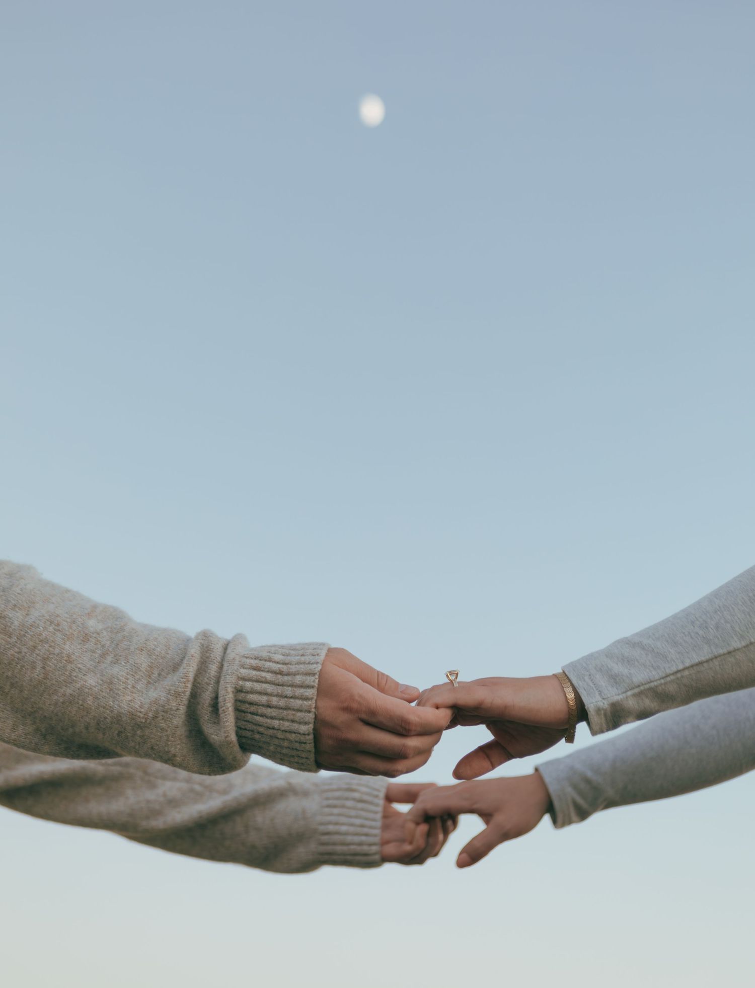 A sequence of hands reaching out to each other against a soft blue sky with a moon in the background.