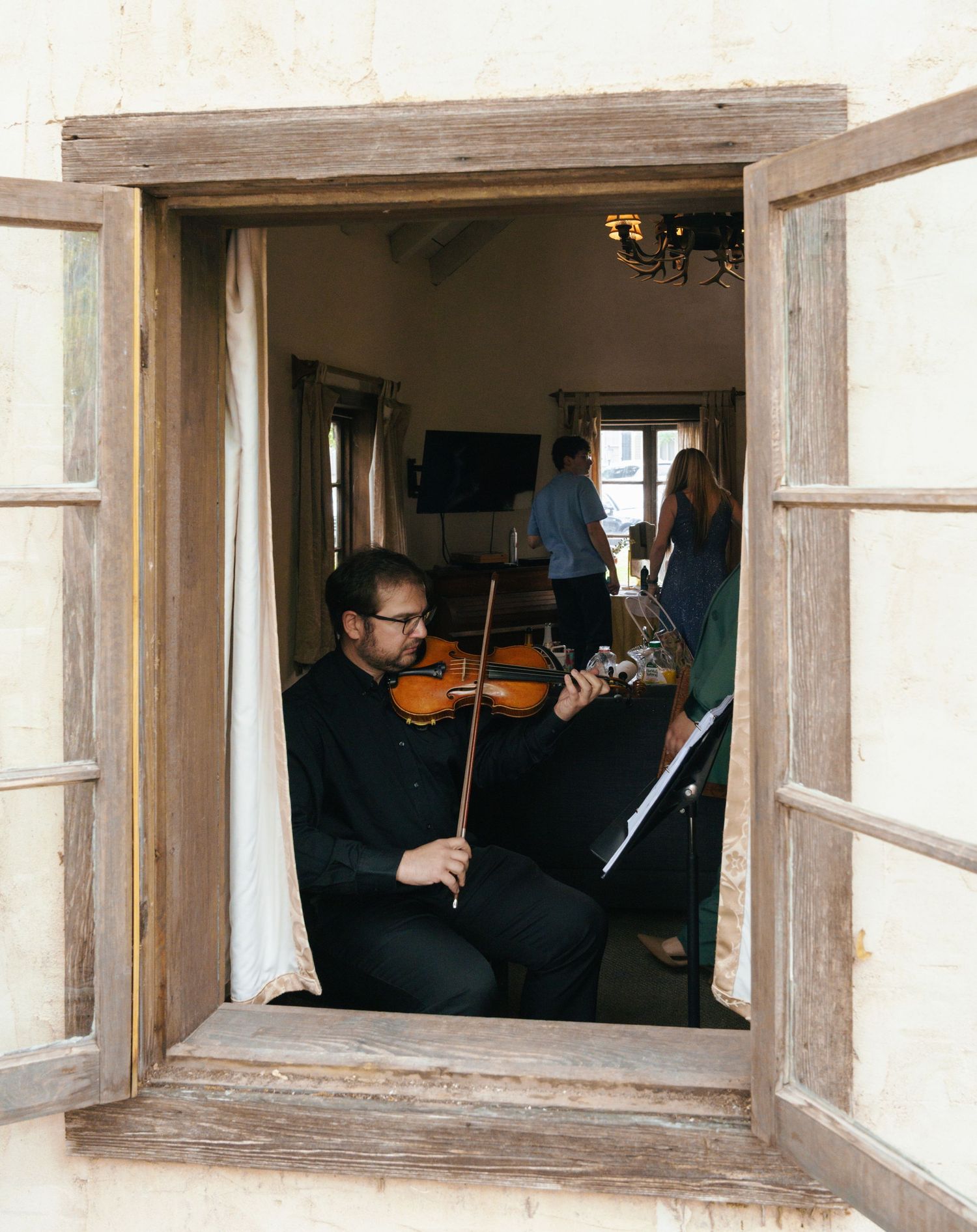 Musicians perform through open windows in a rustic building, playing string instruments in a creative arrangement.
