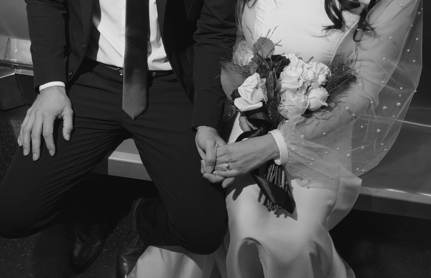 Black and white close-up of wedding attire showing a bouquet and formal wear details.