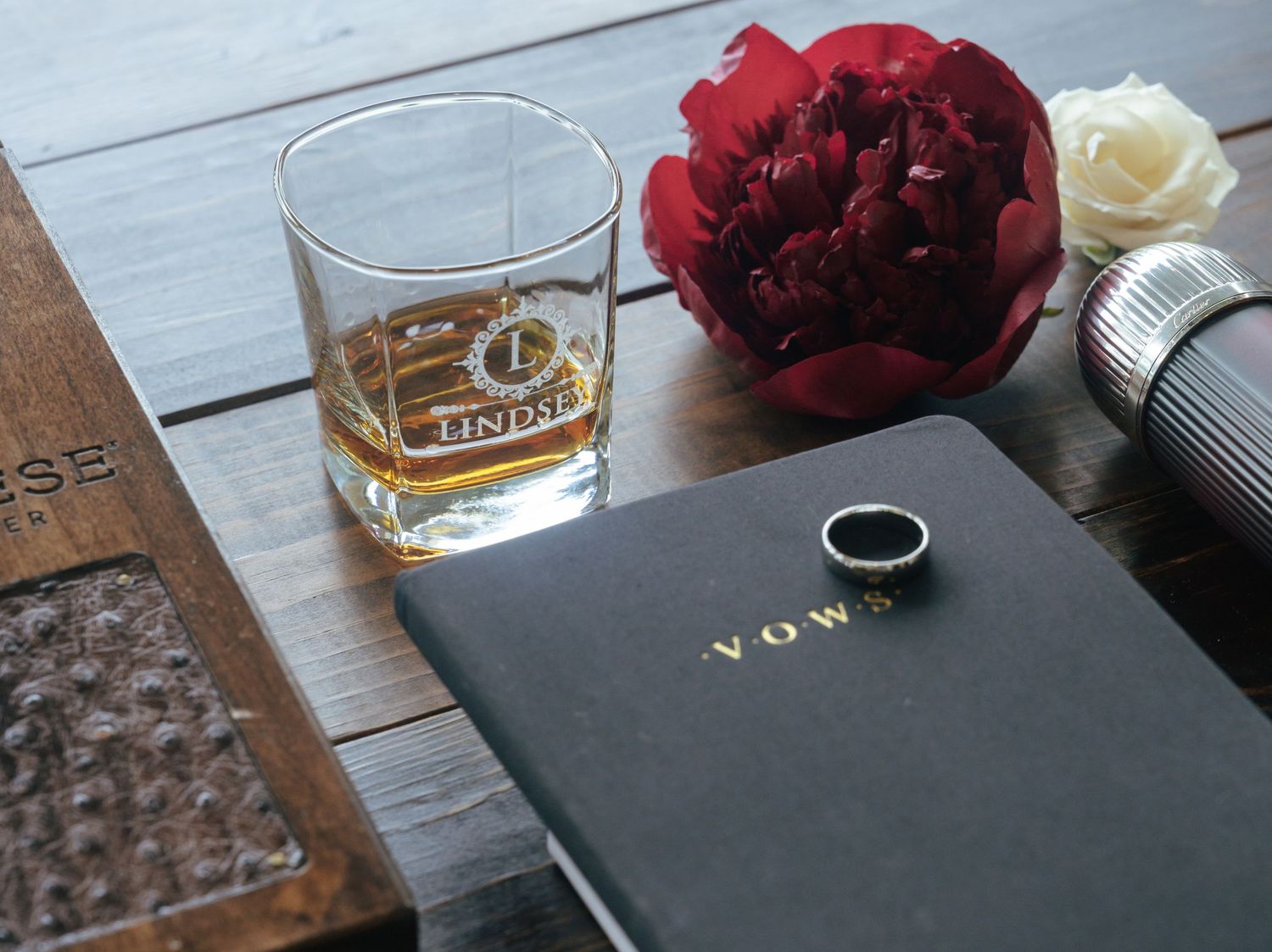 Wedding details with red flowers and drinks on a wooden surface.
