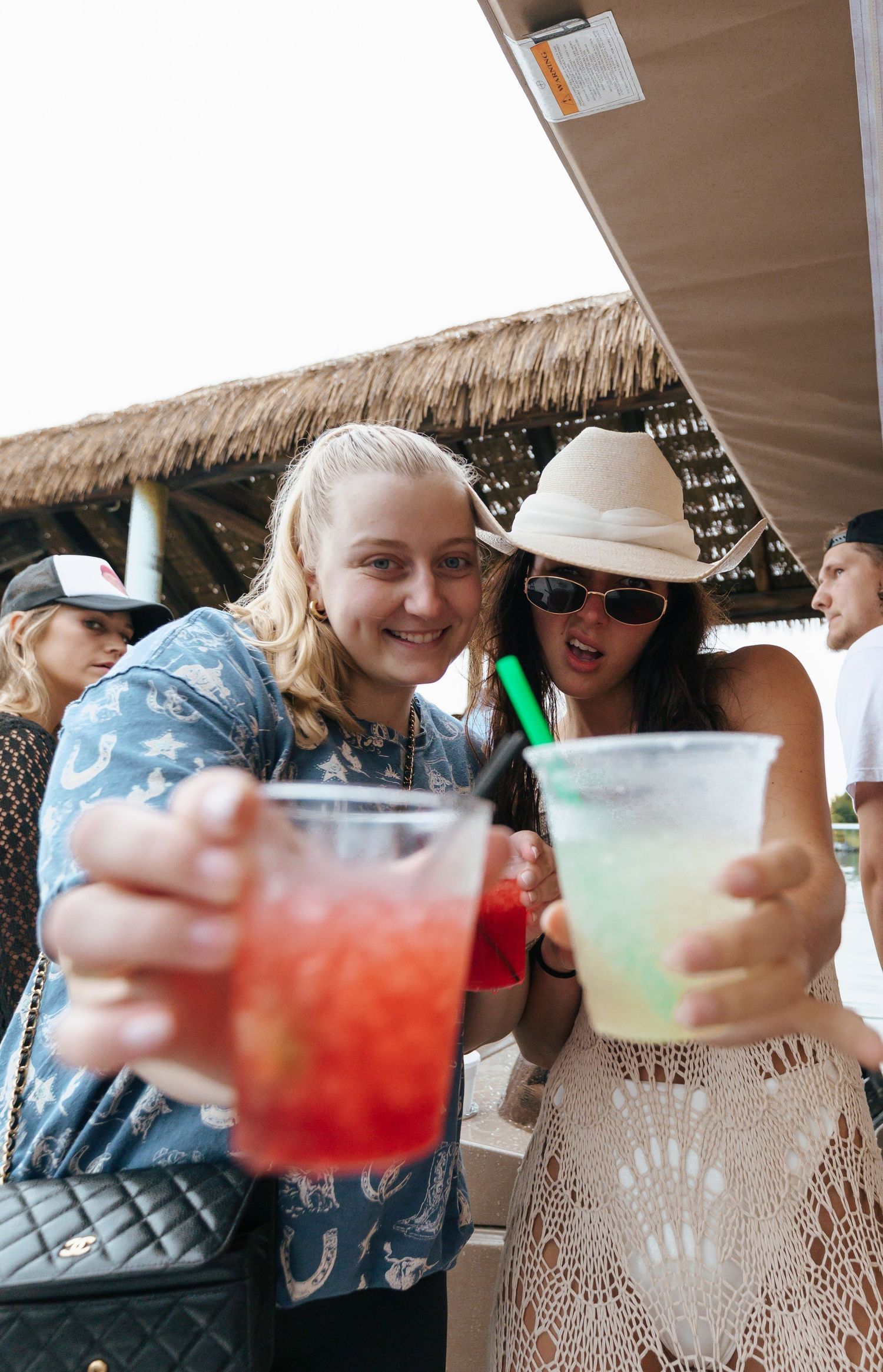 Colorful tropical cocktails being held up in a toast at a tiki bar with thatched roof decor.