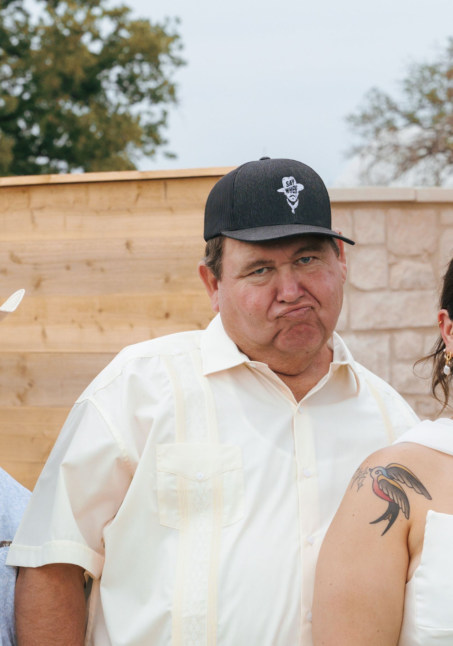 A person wearing a white shirt and baseball cap makes an expressive face in a series of five similar photos.