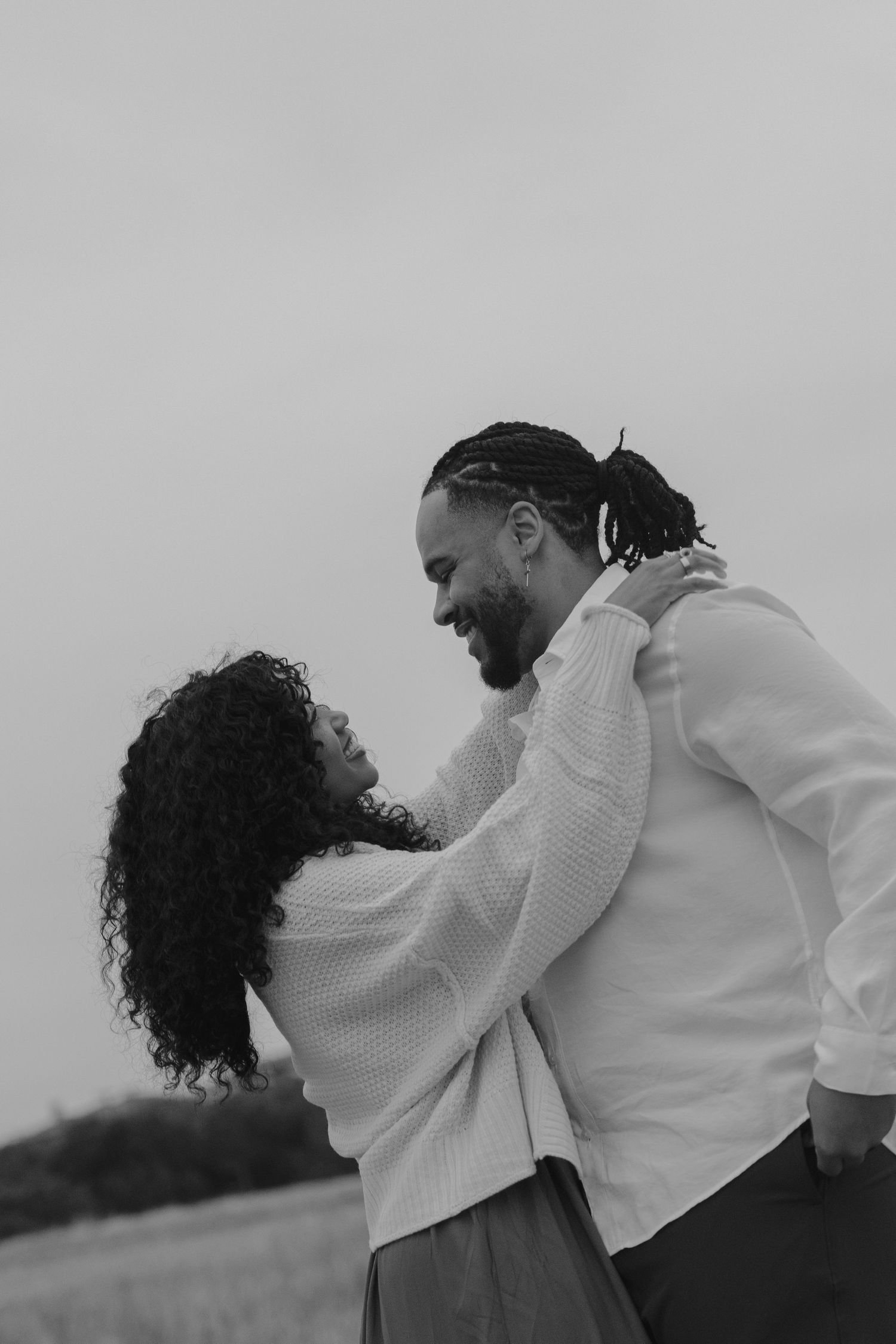 A romantic black and white photo series showing a couple in white outfits embracing and dancing together outdoors.