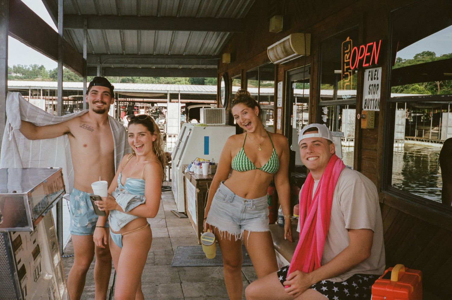 A group of people in summer attire walking through a covered outdoor walkway at a marina or dock area.