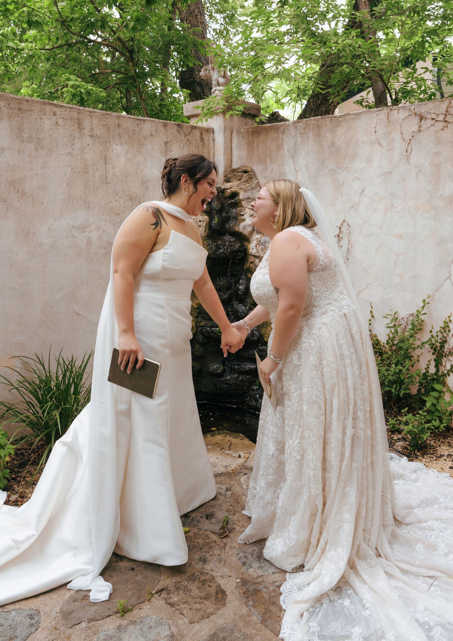Two people in white wedding dresses share an intimate moment in a garden setting during a special celebration.