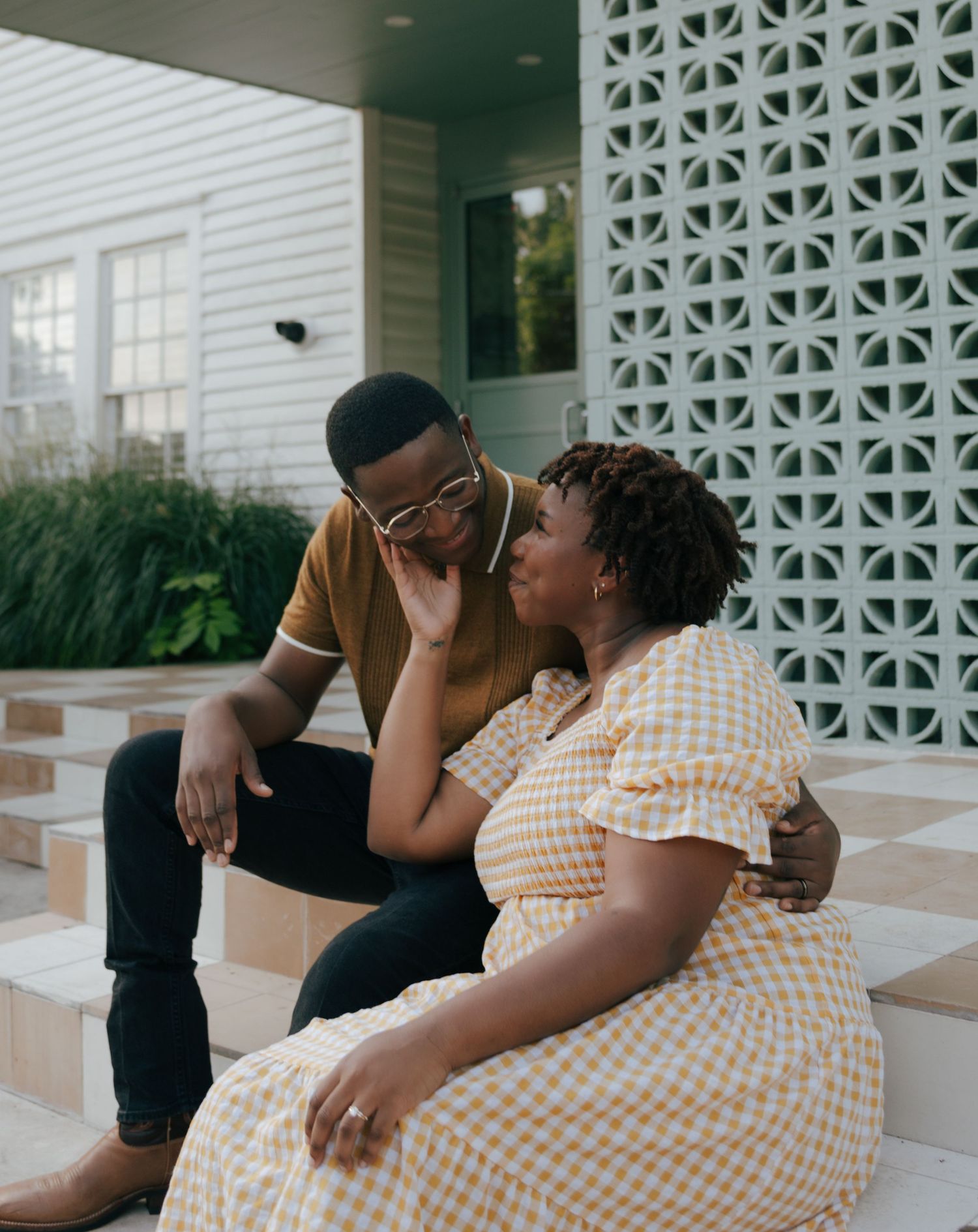 Couple in casual attire sharing intimate moments on outdoor porch steps.