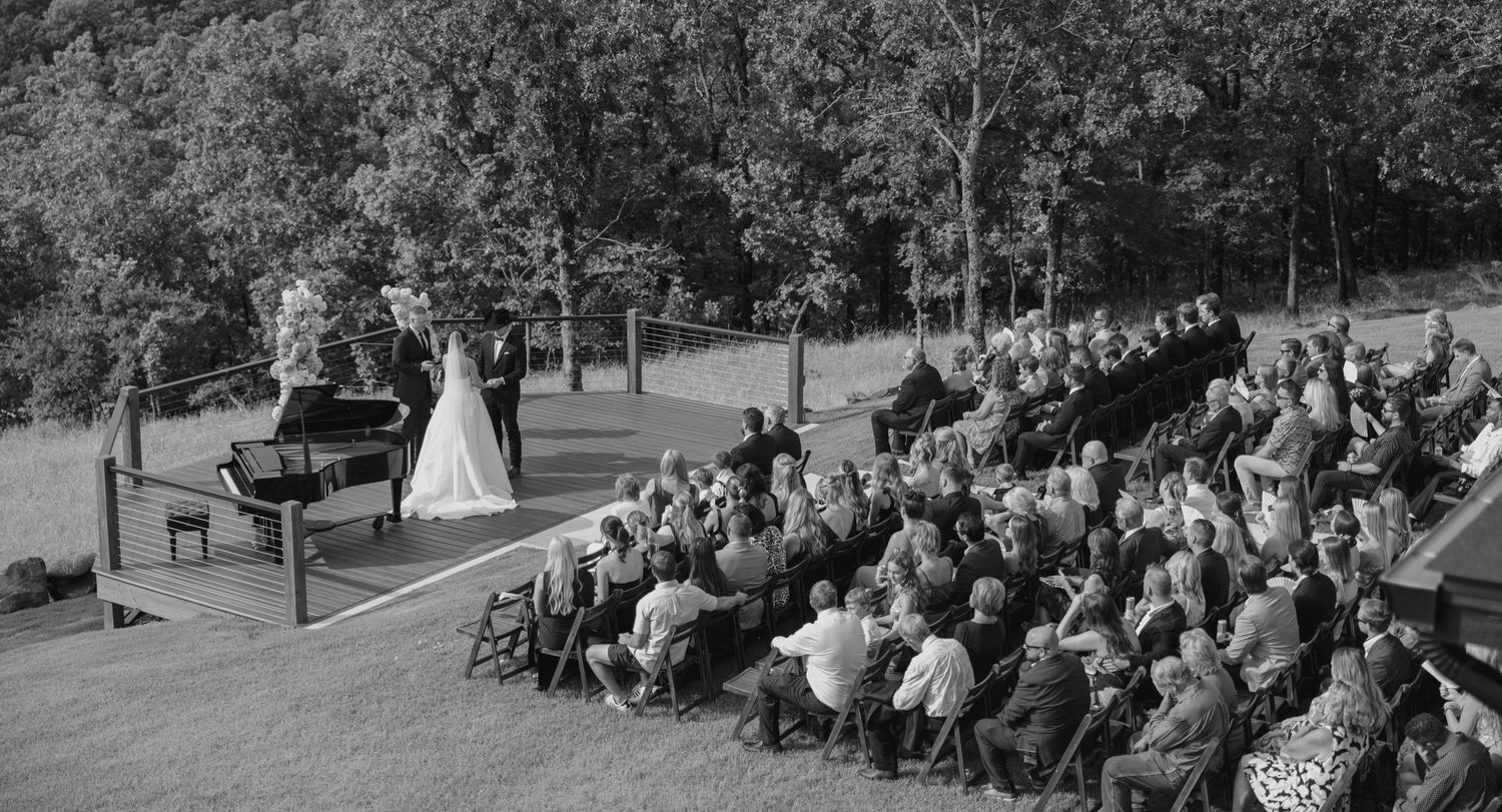Wide angle view of wedding guests seated in rows at outdoor ceremony.
