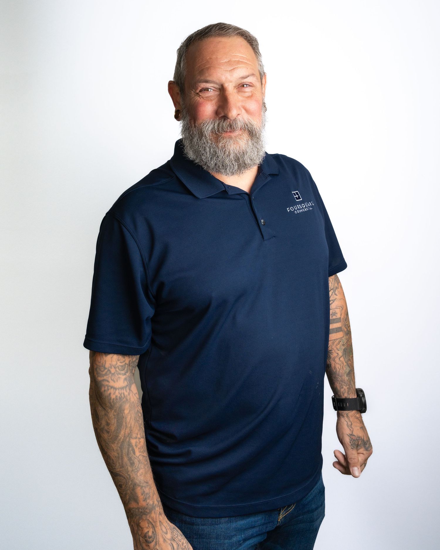 A person in a navy blue polo shirt with visible tattoos on their arms poses against a white background.