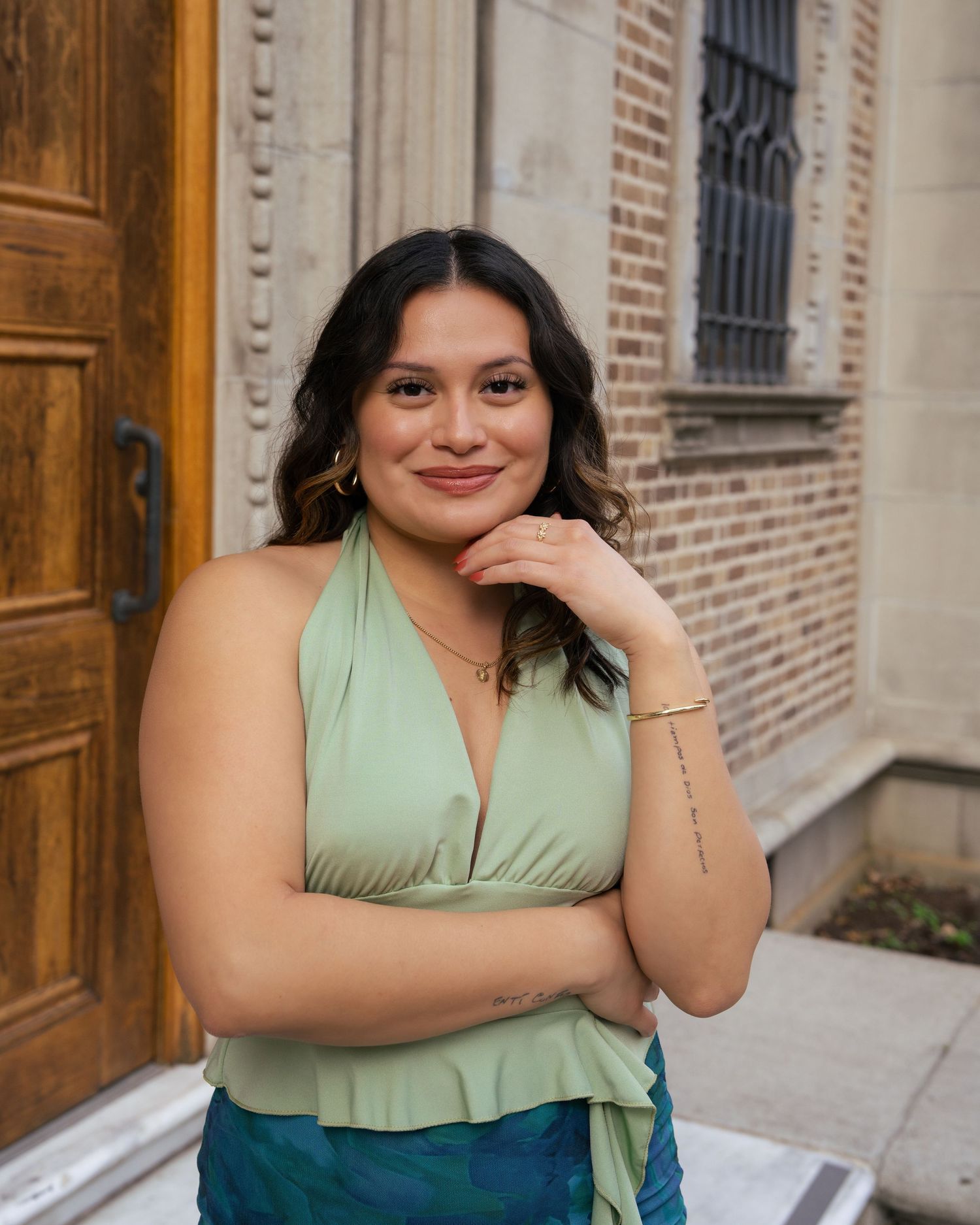 A person in a mint green dress poses against a brick wall with wooden doors in an outdoor setting.