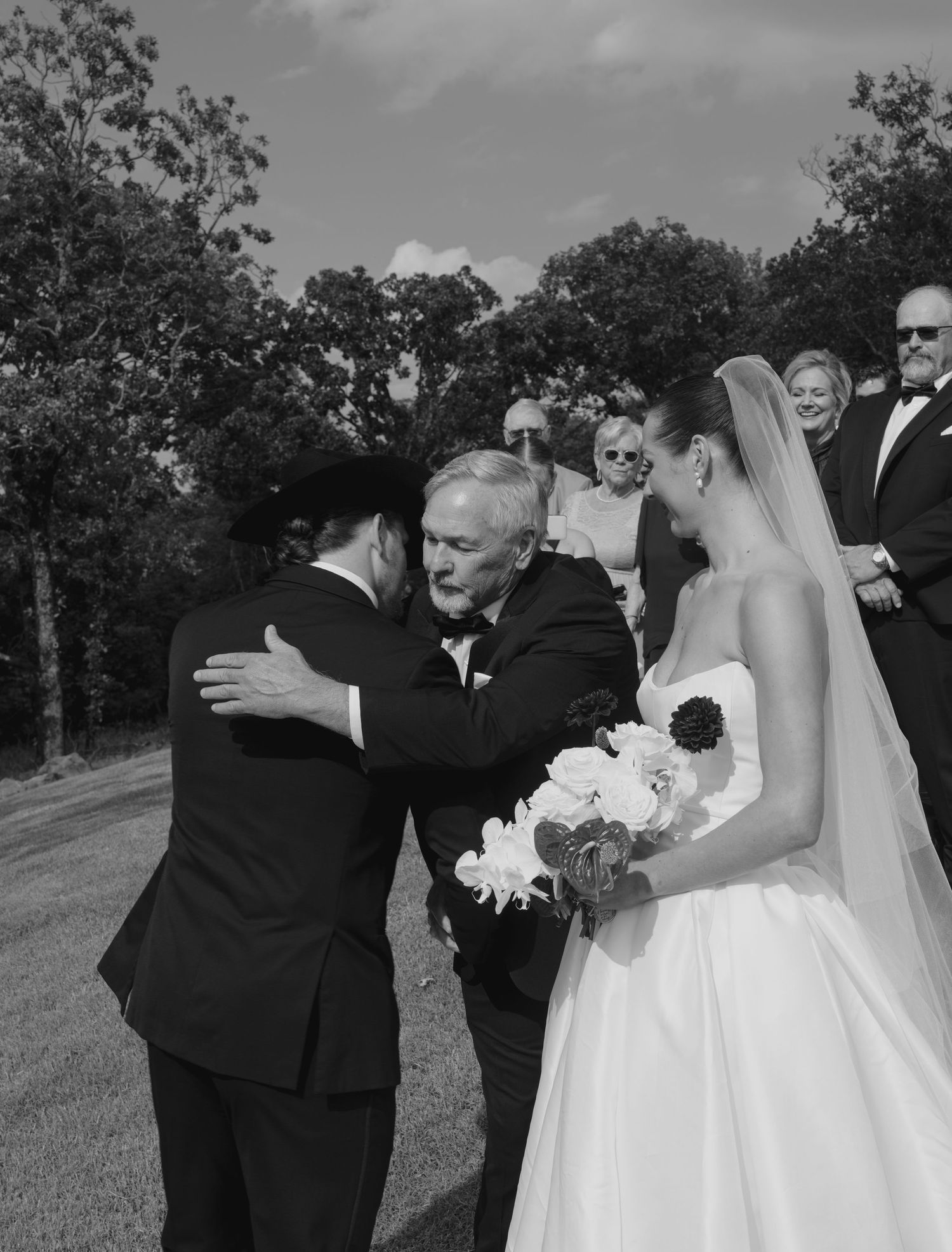 Outdoor wedding ceremony with guests gathered on a hillside under trees.
