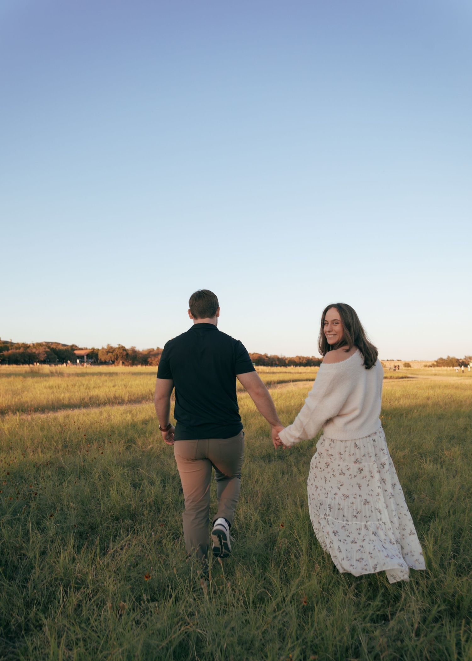 A couple walks hand in hand through a golden field at sunset, creating a romantic silhouette against the horizon.
