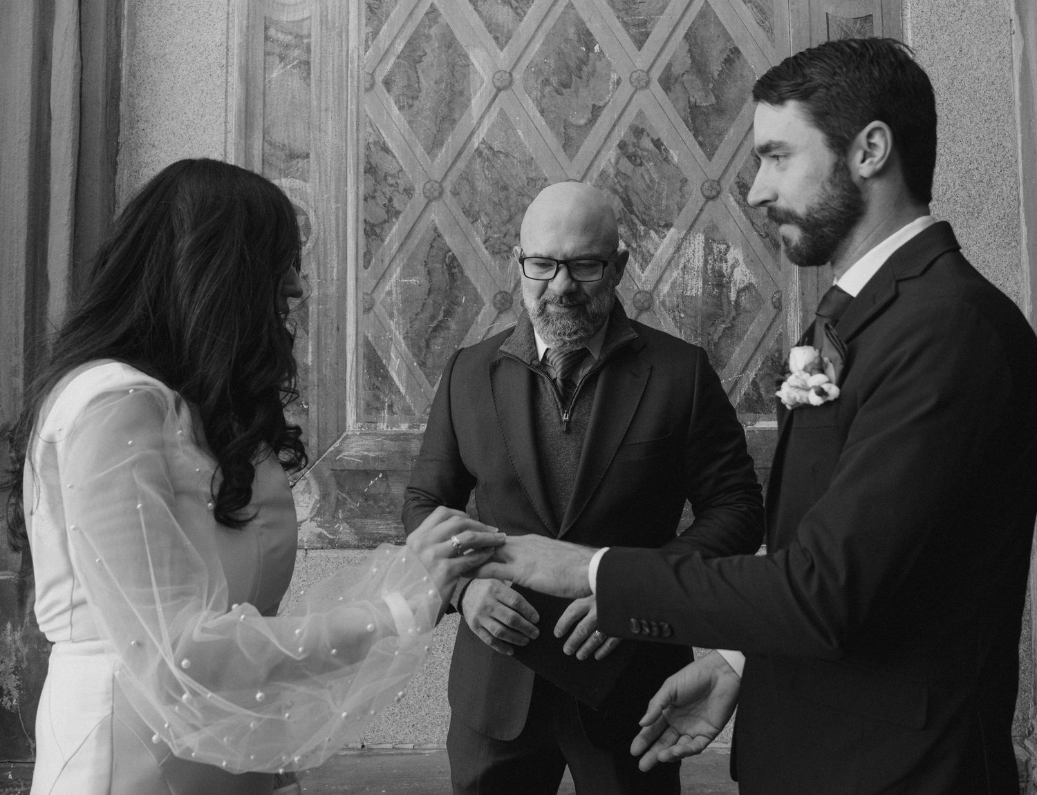 A black and white photograph of a wedding ceremony with a couple exchanging rings in front of an officiant.