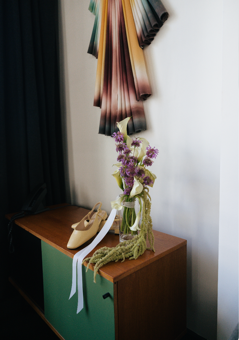 Vintage green dresser topped with cream ballet flats, purple wildflowers in a vase, and colorful fabric wall art above.