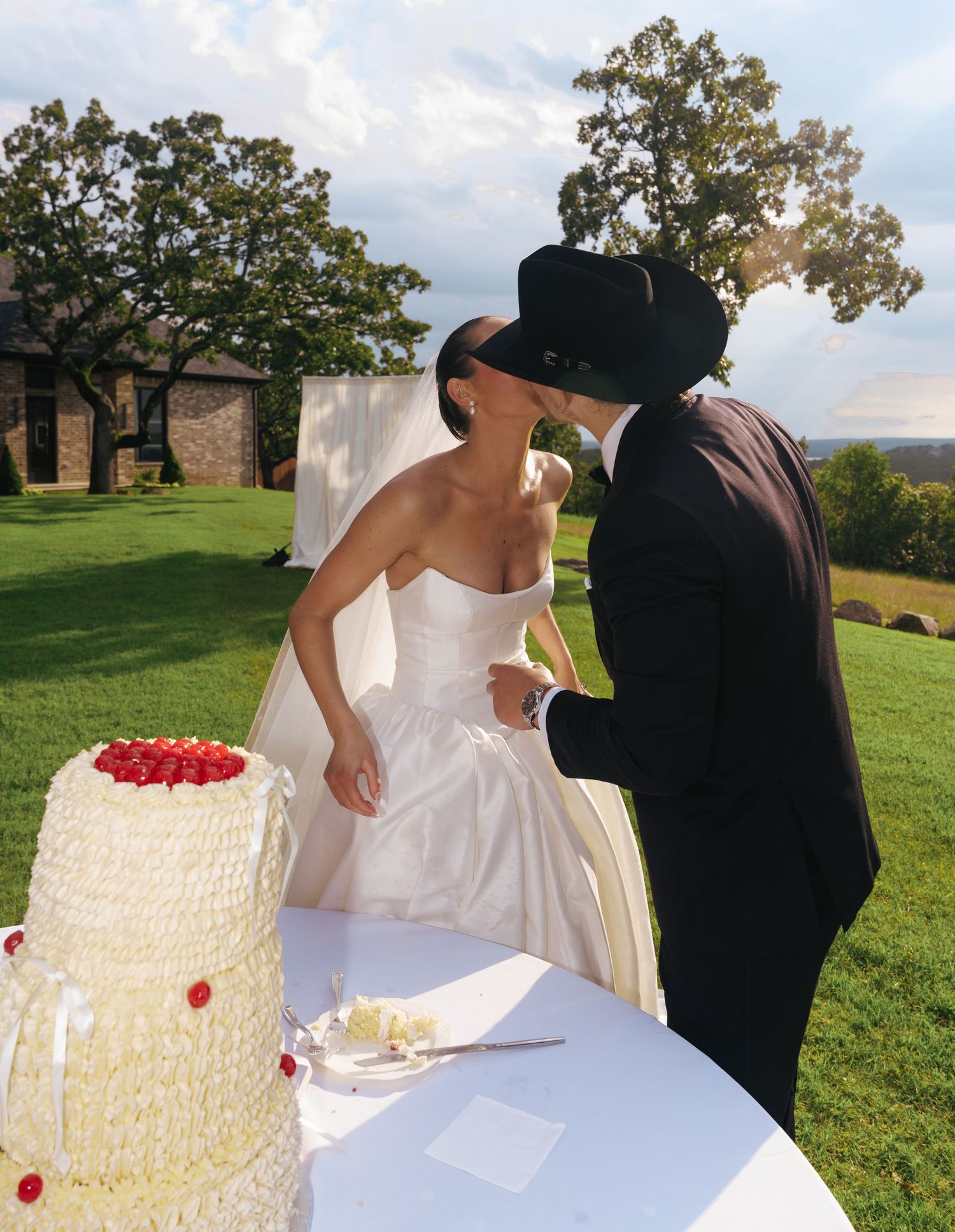 A candid moment between newlyweds sharing laughter by their wedding cake outdoors.