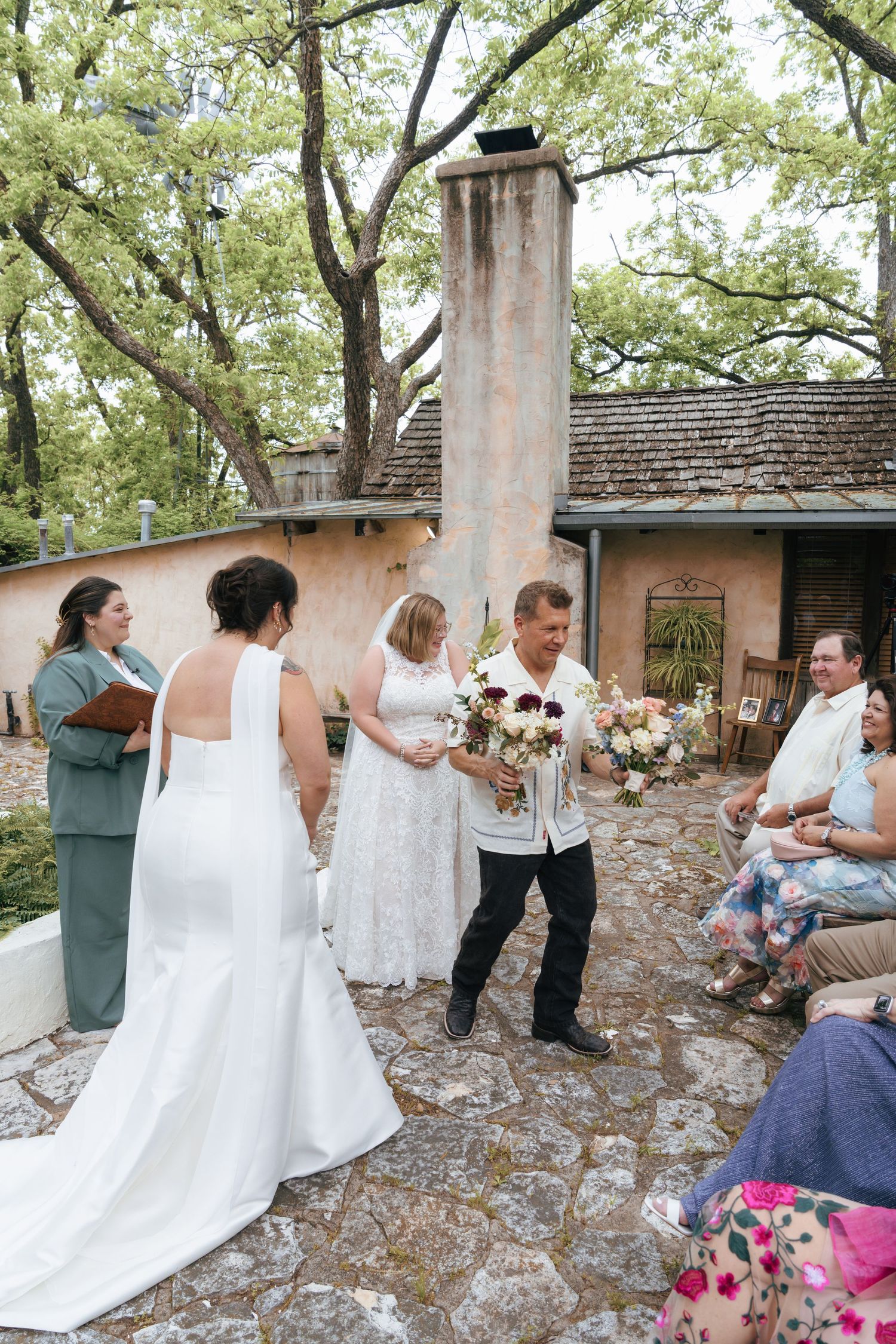 Group of people in white attire dancing and celebrating at an outdoor stone patio gathering.