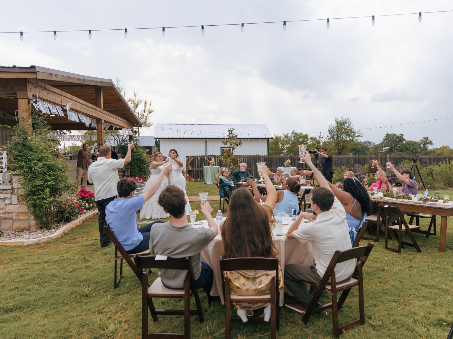 A panoramic view of outdoor dining tables arranged on a lawn with guests enjoying a meal in a rustic setting.