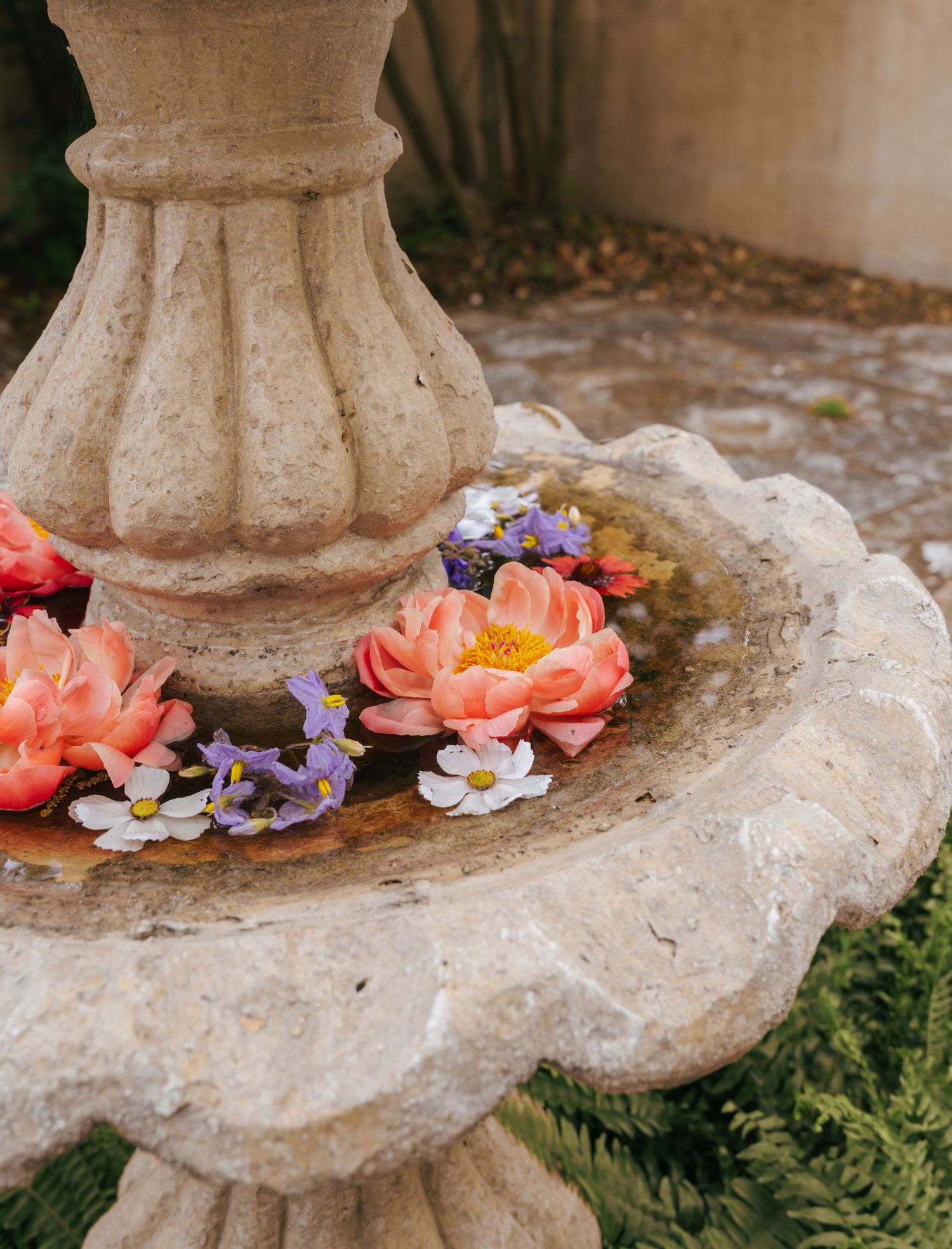 Delicate coral and purple flowers artfully arranged around the base of a weathered stone garden pedestal.