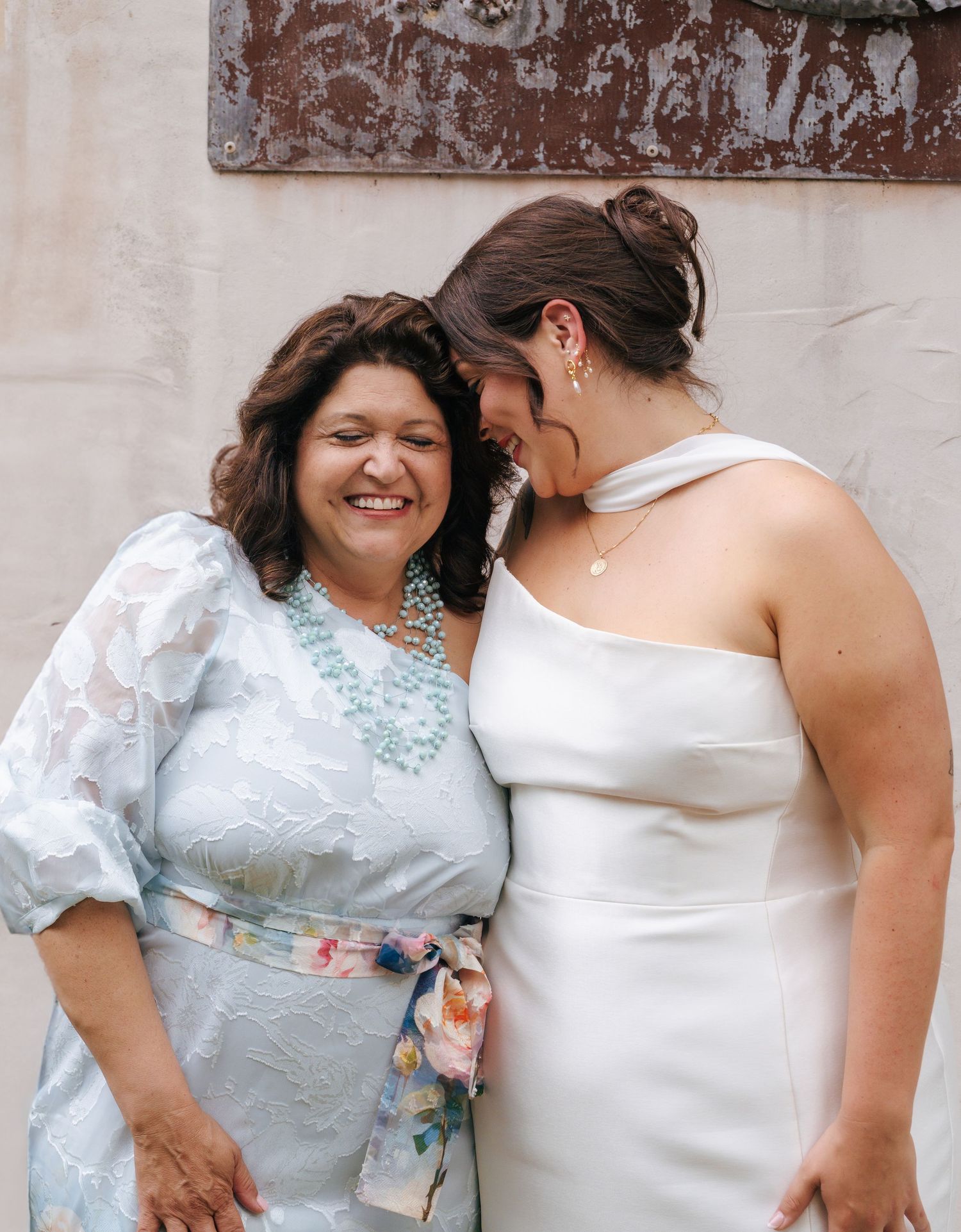 Two people share a joyful moment together while wearing a white dress and light blue floral outfit.