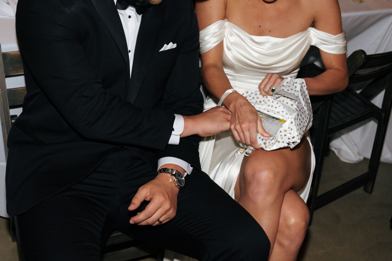 Newlyweds share intimate moment at reception table in formal attire.