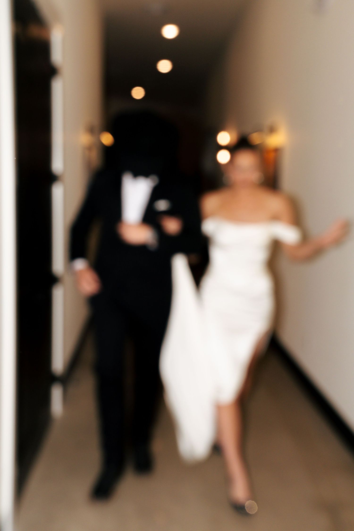 Bride and groom playfully dance in a hotel hallway during their wedding reception.