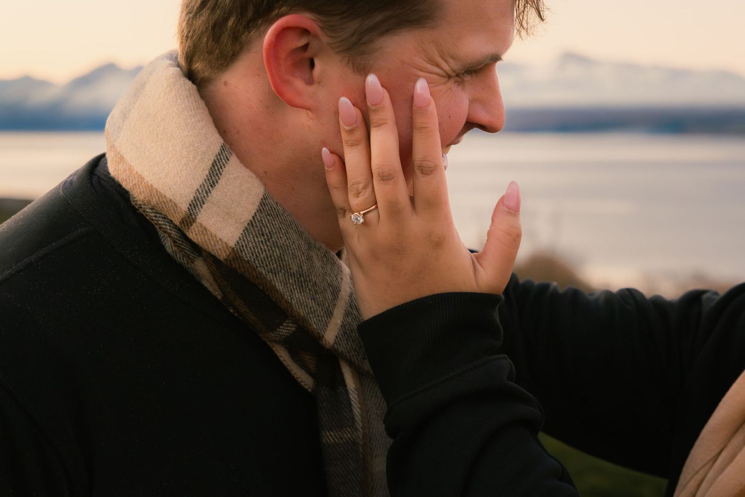 Romantic close-up of newly engaged couple, woman touching man's face with diamond ring visible.