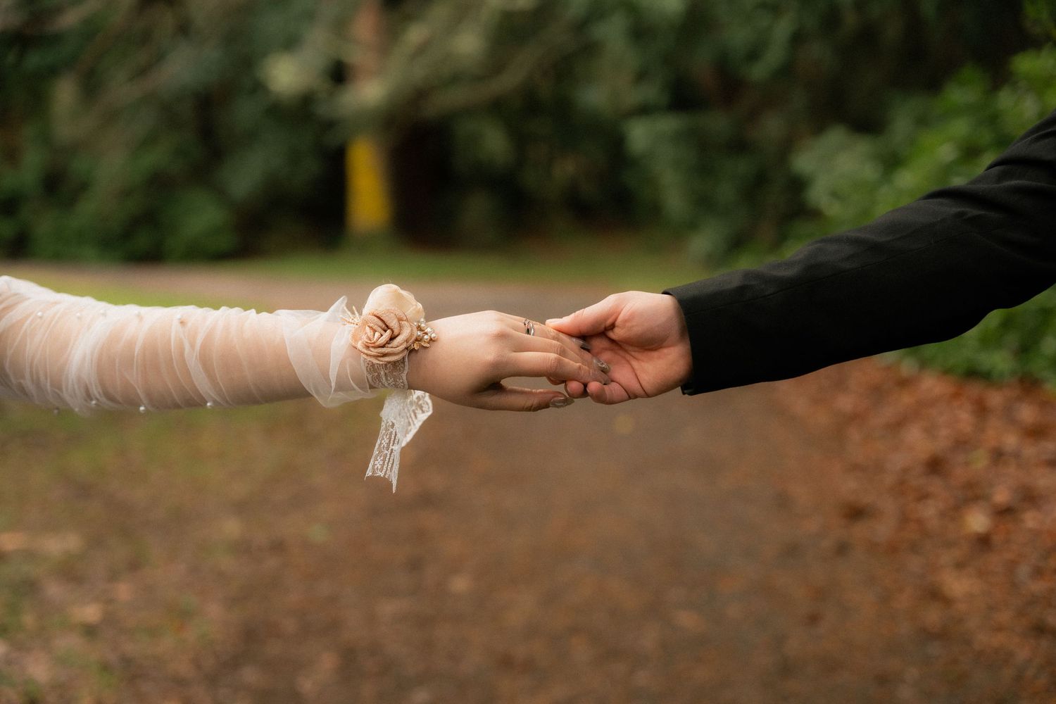 Close-up of a bride and groom gently holding hands outdoors, showcasing lace bridal sleeve with floral detail.