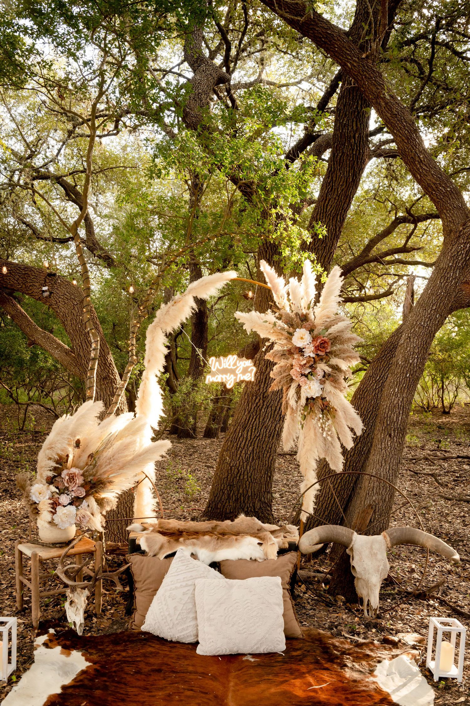 Bohemian styled seating area with white cushions and large paper flower decorations under trees.