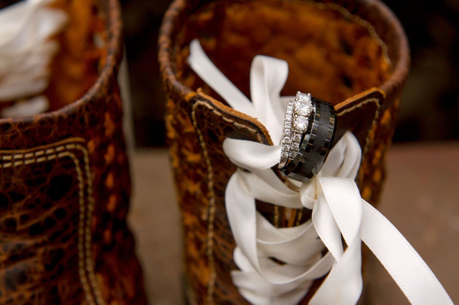 A diamond engagement ring rests on white laces threaded through a brown leather boot.