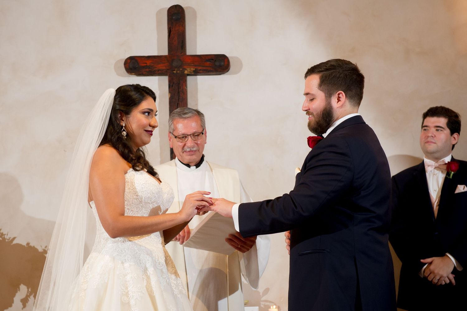 Traditional church wedding ceremony with wooden cross and white walls in background.