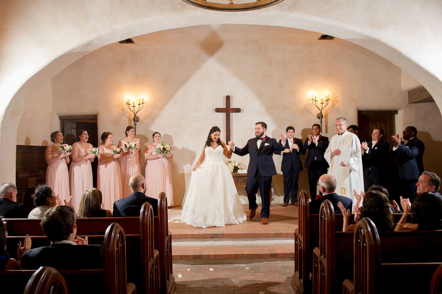 Church wedding ceremony in progress with guests seated in wooden pews under vaulted ceiling.