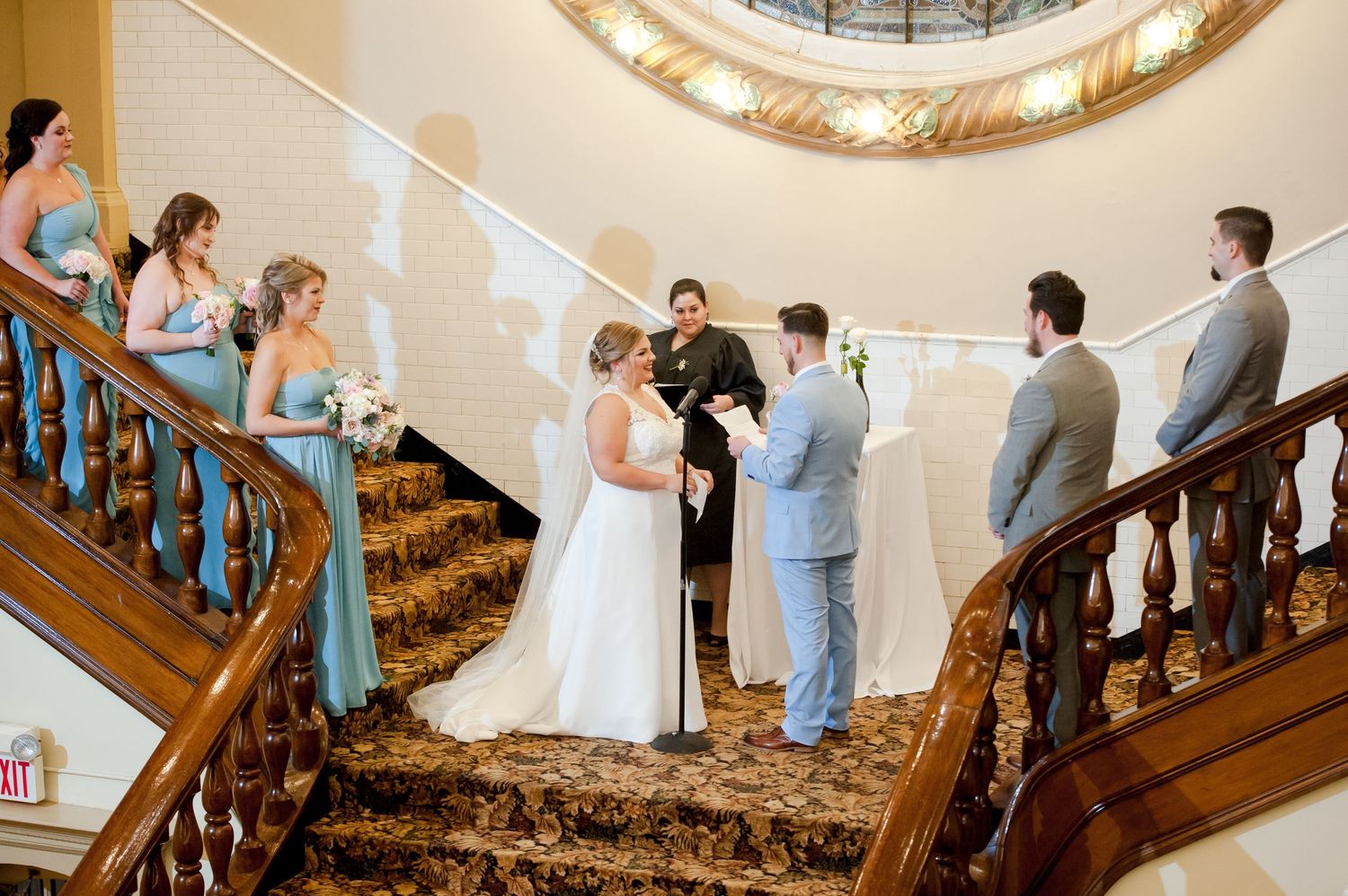Wedding ceremony participants gathered on an elegant staircase under a domed ceiling.