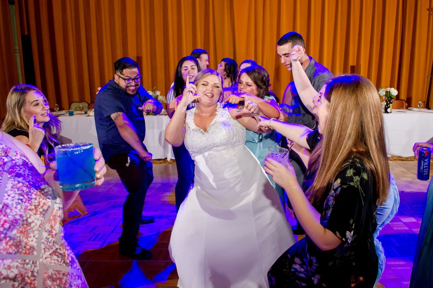 Lively dance floor scene with wedding guests celebrating under blue and purple lighting.