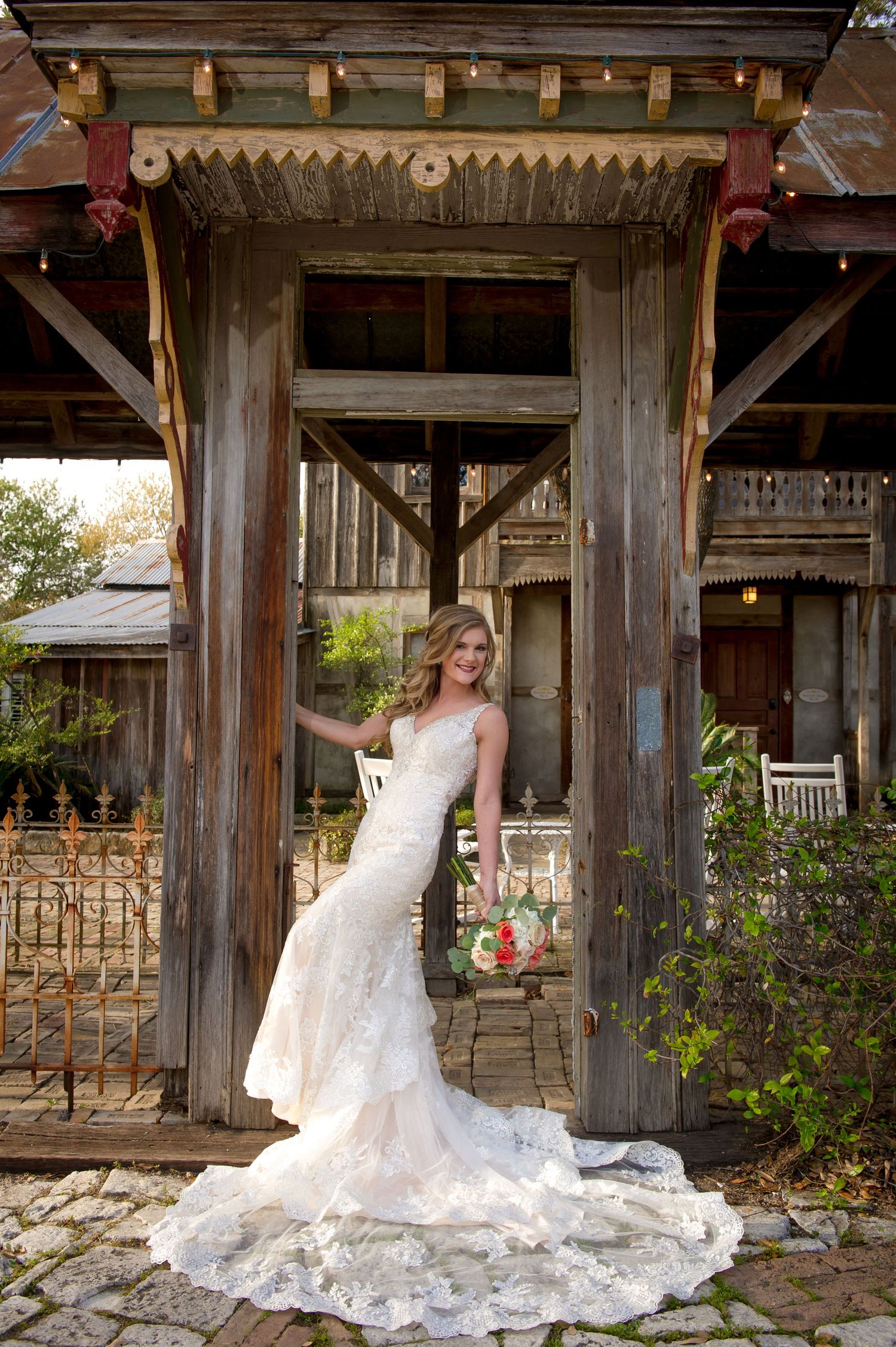Elegant white wedding dress with long train displayed in rustic wooden pavilion setting.