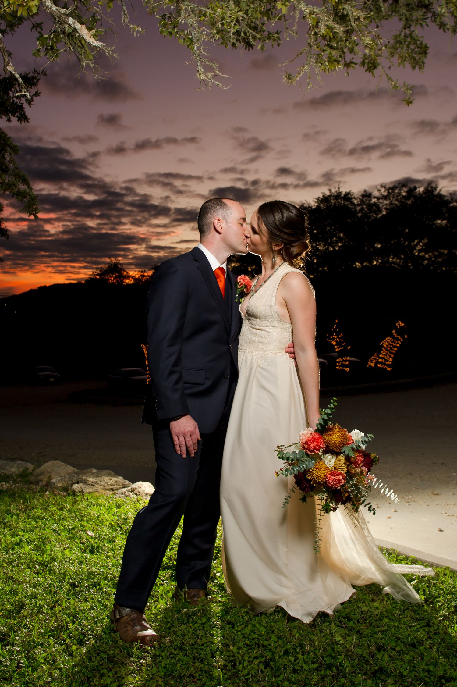 Sunset wedding portrait with dramatic orange sky and natural landscape backdrop.