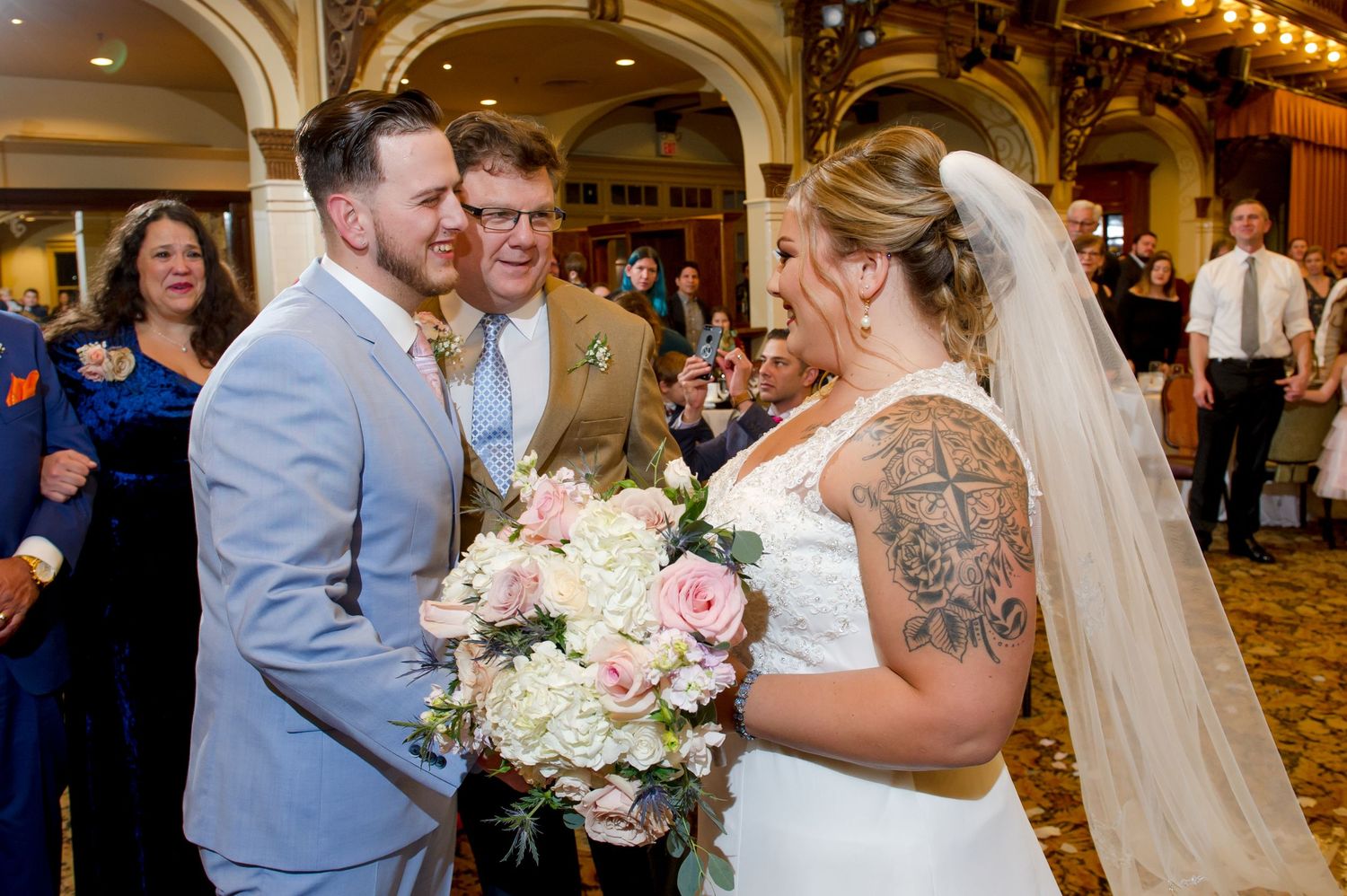 A wedding ceremony in a grand ballroom with bridesmaids in light blue dresses and elegant decor.