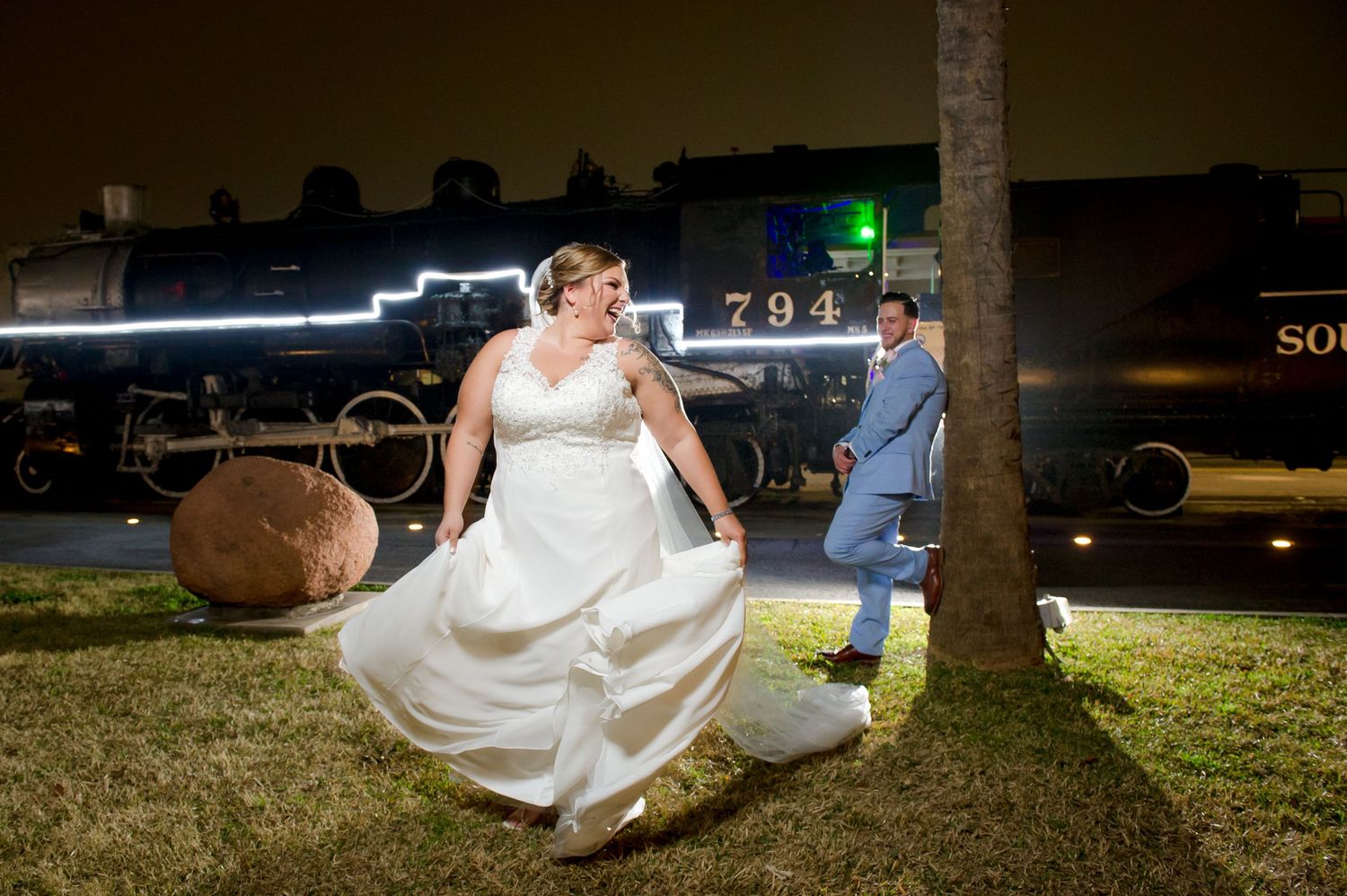 Wedding couple poses on illuminated lawn during evening celebration.