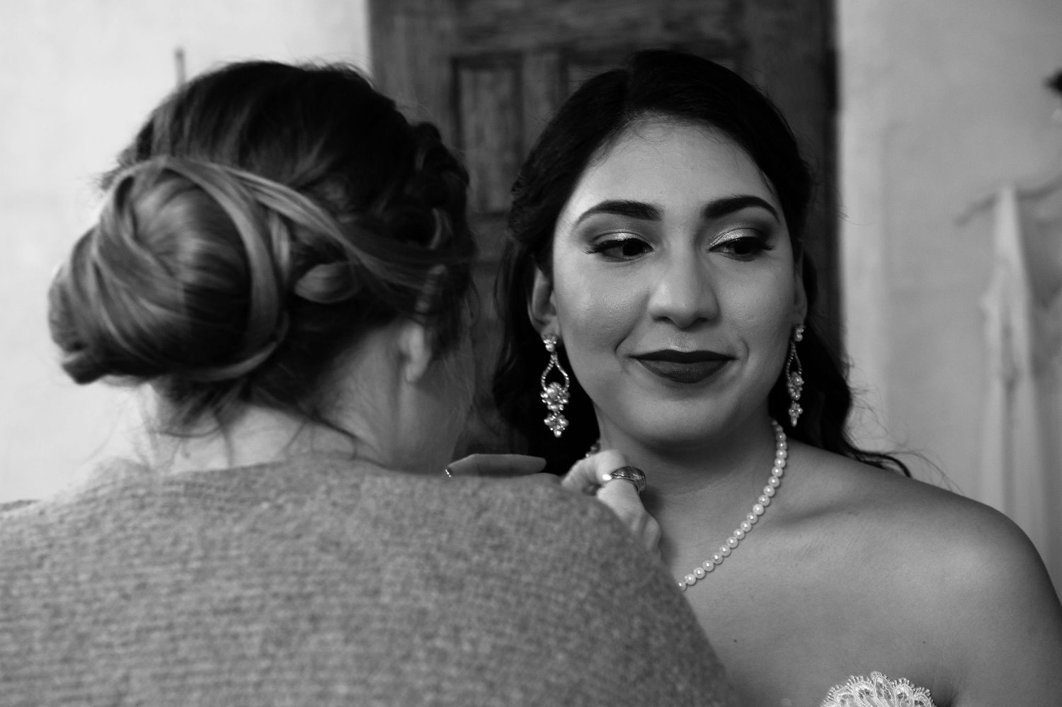 Black and white portrait showing reflection of bride with pearl jewelry in elegant setting.