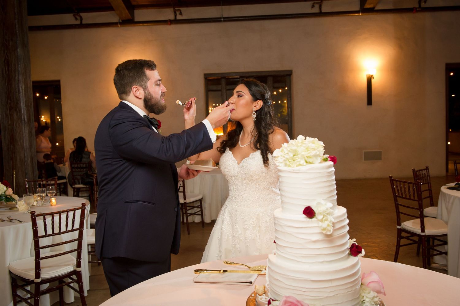 Newlyweds feed each other bites of wedding cake during their reception celebration.