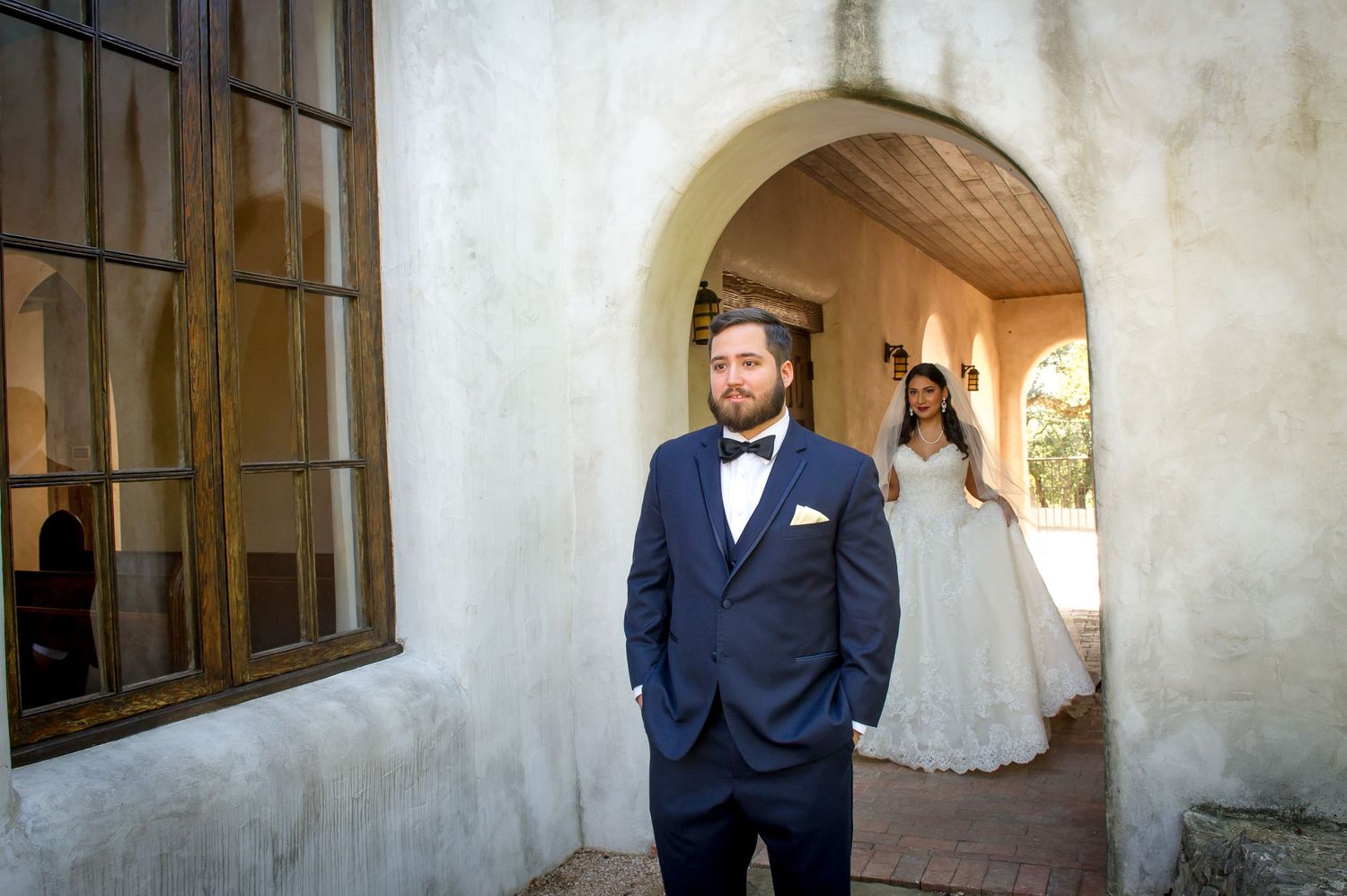 A wedding couple stands in a rustic covered walkway during their first look photo session.