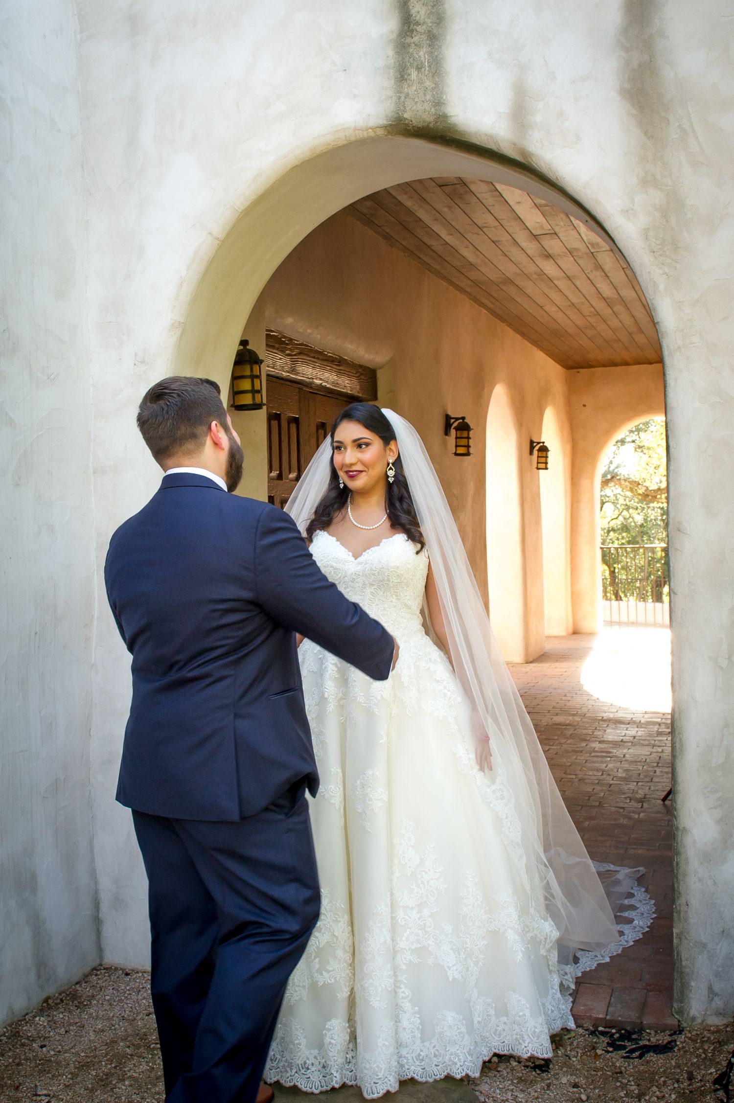 A couple shares an intimate first look moment in a Spanish-style arched corridor.