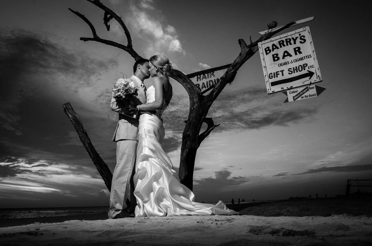 Black and white wedding portraits with a vintage bar sign and dramatic clouds.